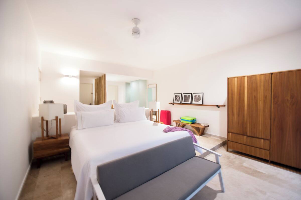 Une chambre d’hôtel moderne comprenant un lit, une table de chevet, une armoire et un petit coin salon.