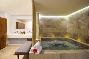 A modern bathroom with a stone wall, a bathtub, a vanity with a mirror, and a bench with towels.