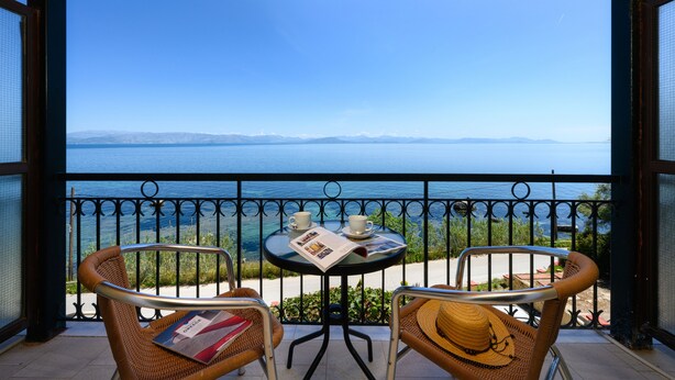 A balcony with wicker chairs, a table with a newspaper, and a view of the sea. - Batelo Boutique Hotel - Adults Only (Corfu)