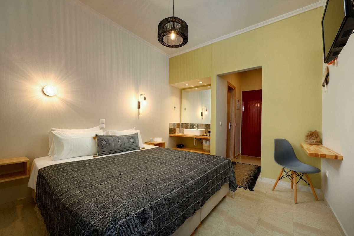Un dormitorio con cama, mesitas de noche, una silla, un espejo y televisión.
