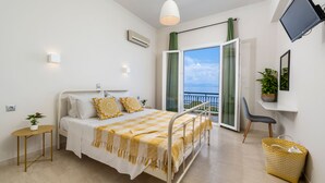A bedroom with a bed, bedside table, lamp, potted plant, and a view of the outdoors. - Batelo Boutique Hotel - Adults Only (Corfu)