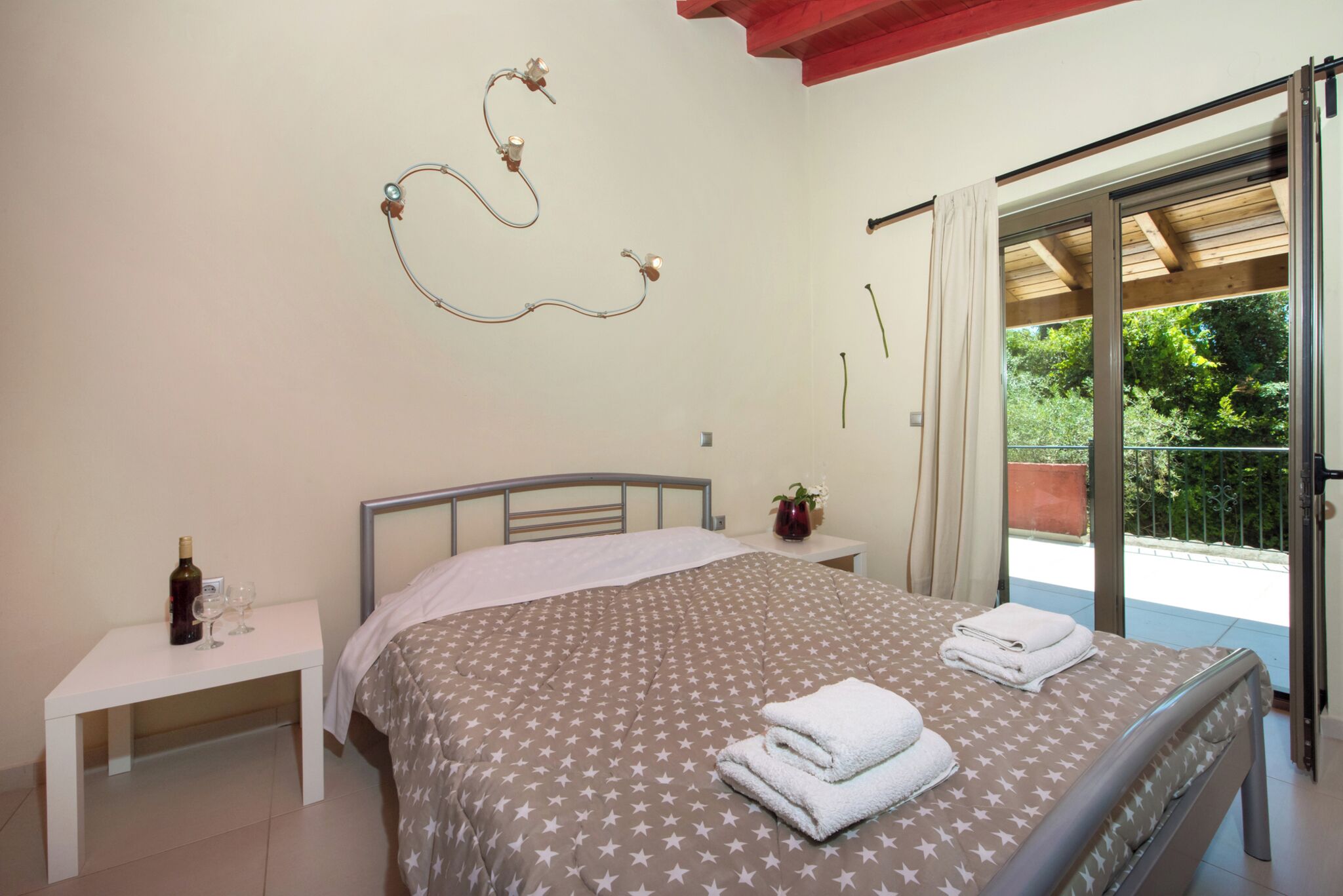 Un dormitorio con cama, mesita de noche, una botella de vino y vistas al exterior.