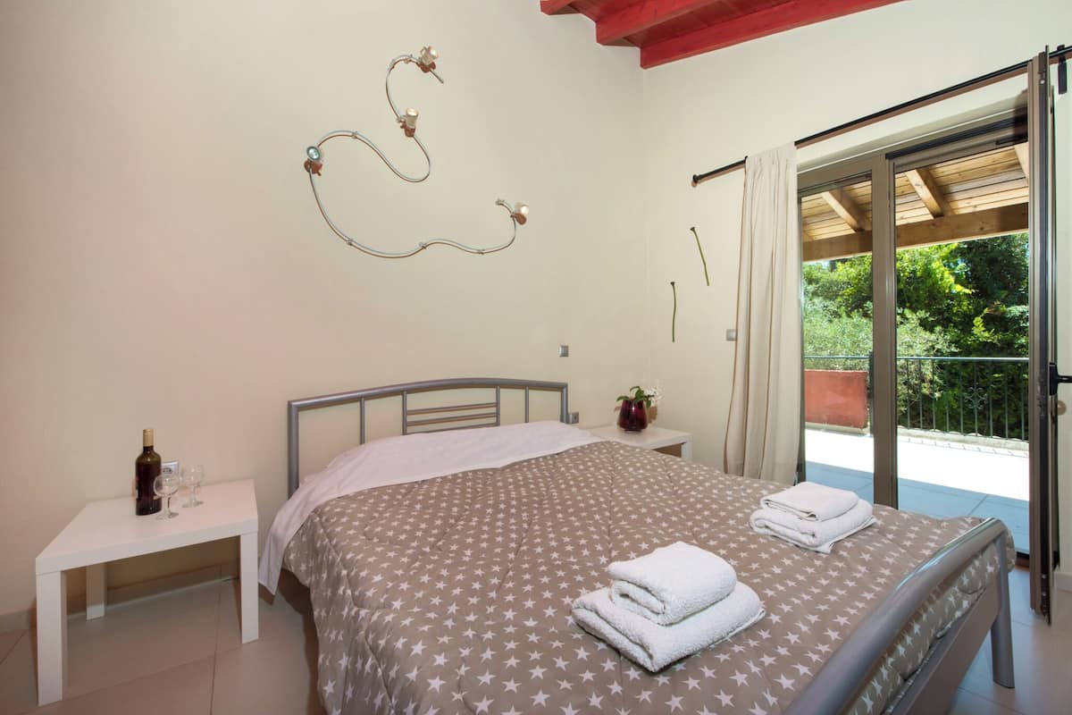 Un dormitorio con cama, mesita de noche, una botella de vino y vistas al exterior.