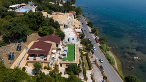 An aerial view of a coastal property with a swimming pool, tennis court, and a road leading to the beach. - Batelo Boutique Hotel - Adults Only (Corfu)