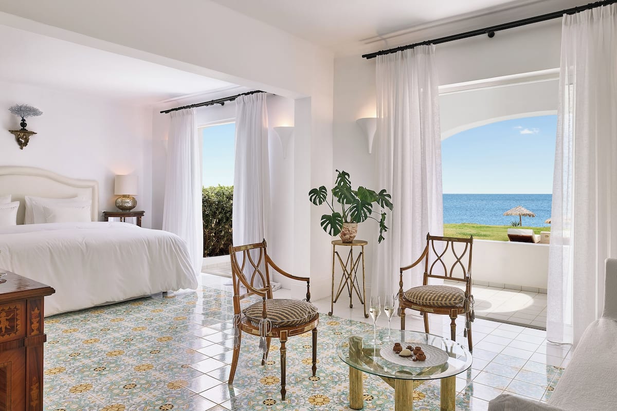 Habitación de hotel con cama, dos sillas, una mesita con bebidas y vista al mar.