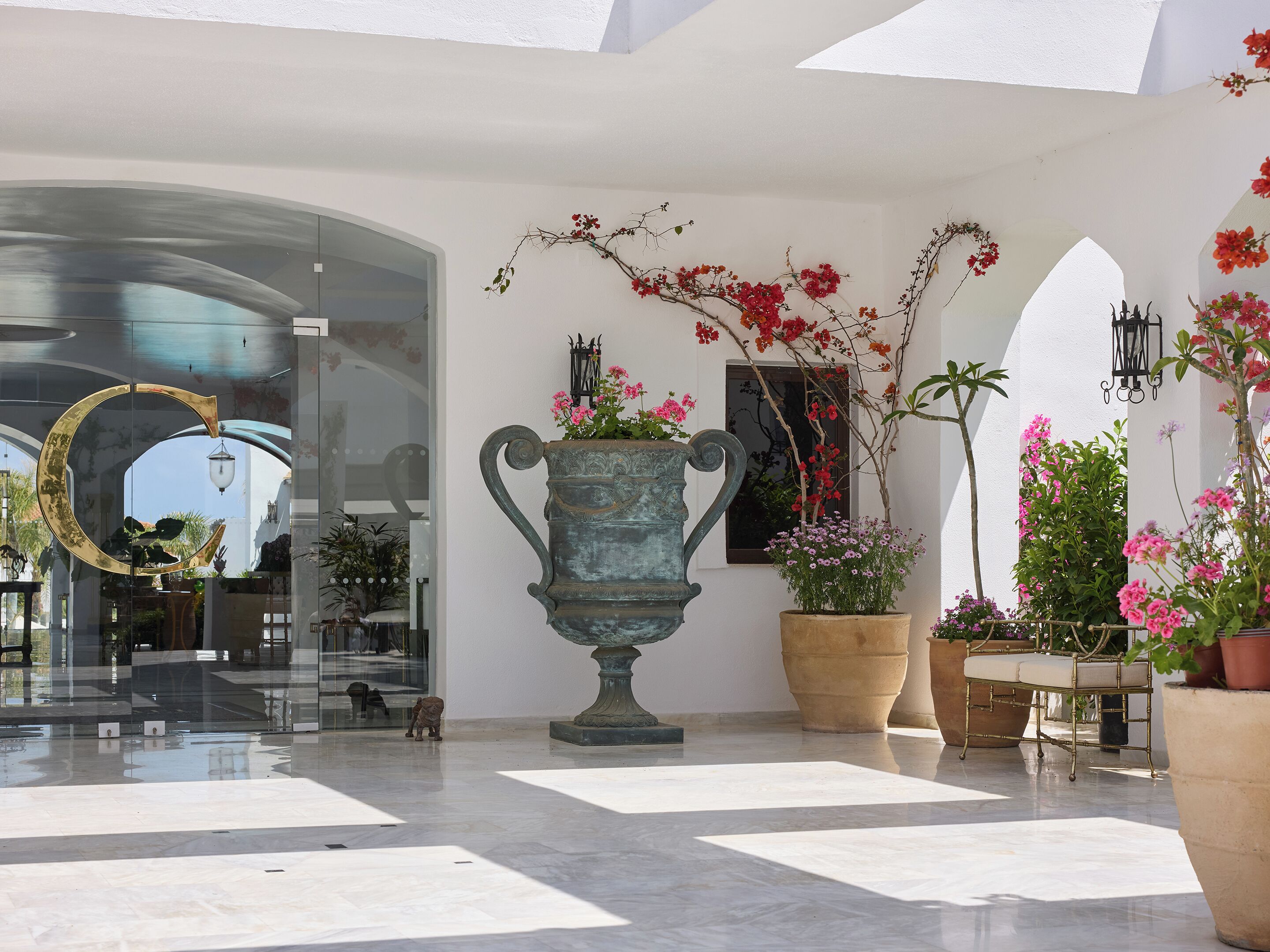 A spacious lobby with a large decorative urn, potted plants, and a glass entrance.