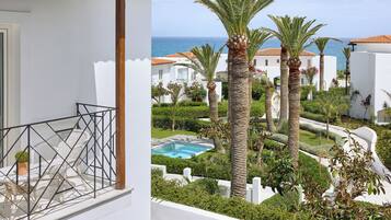Un balcon donnant sur une piscine et des palmiers, entouré de bâtiments blancs aux toits recouverts de tuiles rouges.