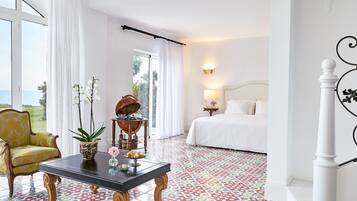 A hotel room with a bed, a sitting area with a table, a chair, and a view of the sea.