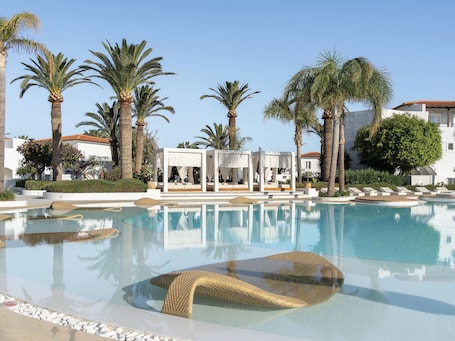 Una piscina al aire libre, sombrillas, sillones reclinables de piscina