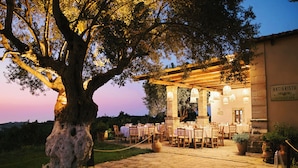 An outdoor dining area with stone flooring, tables set for dining, and a pergola with hanging lights.
