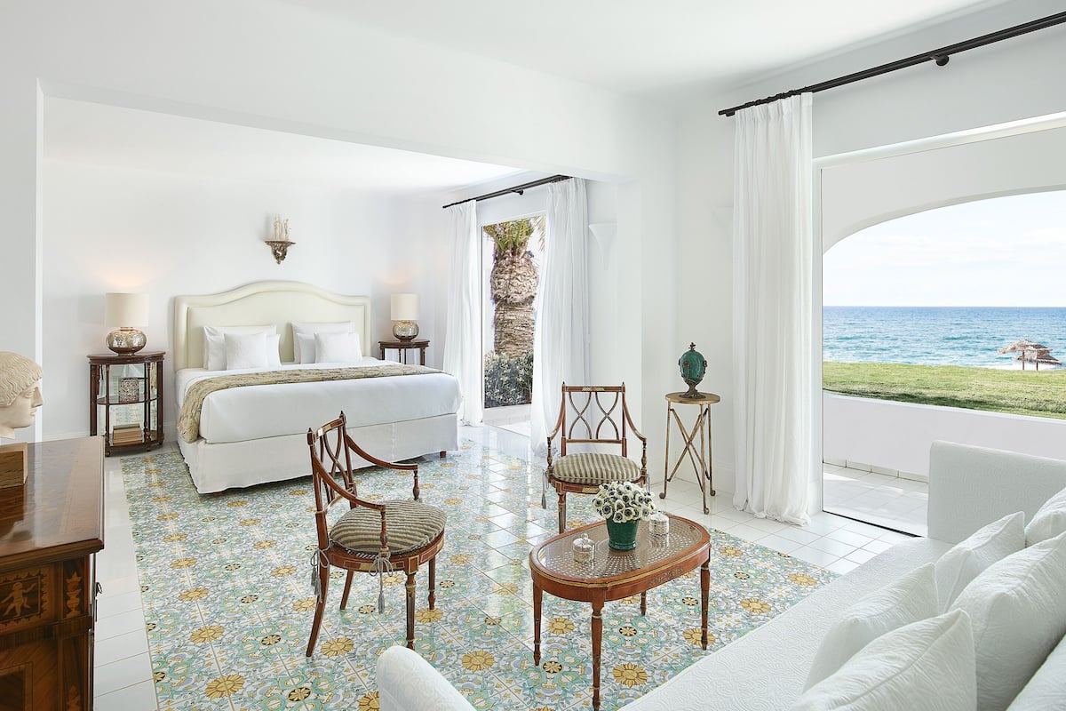 Habitación de hotel con cama, dos sillas, una mesita y vista al mar.