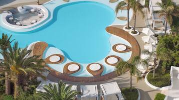 A large, circular swimming pool with multiple seating areas and palm trees.