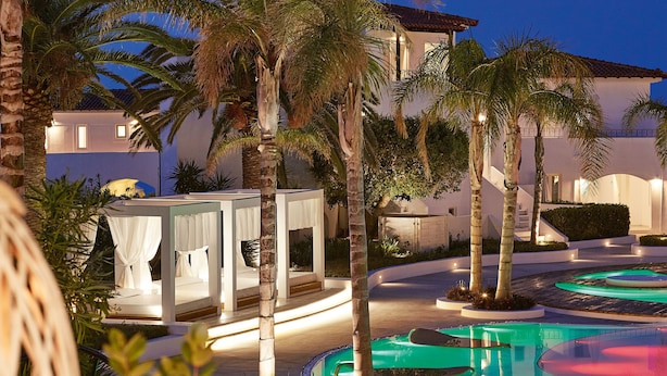 A resort with a pool, palm trees, and a building with a balcony.