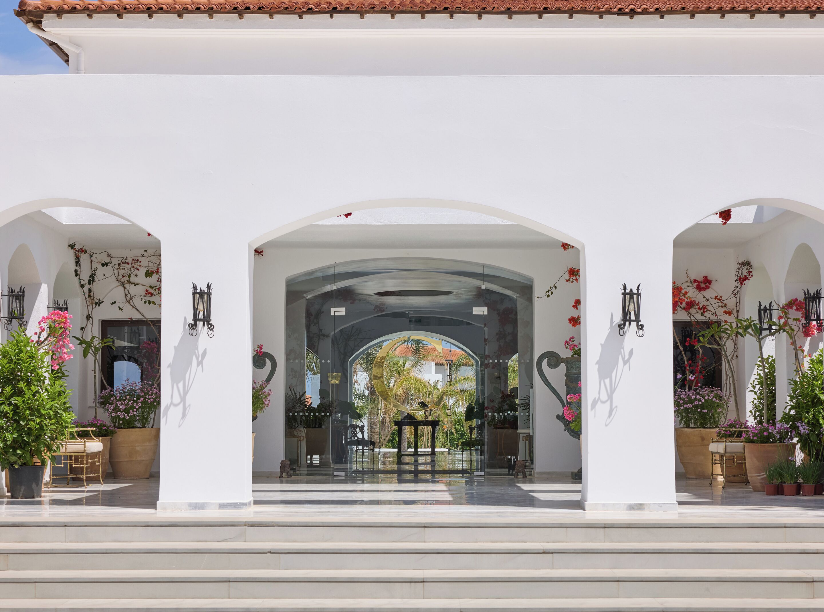 A white building with arches, potted plants, and outdoor furniture.