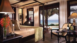 Un espacioso dormitorio con cama con dosel, una zona de estar con vistas al océano y una mesa de comedor con una botella y una copa.