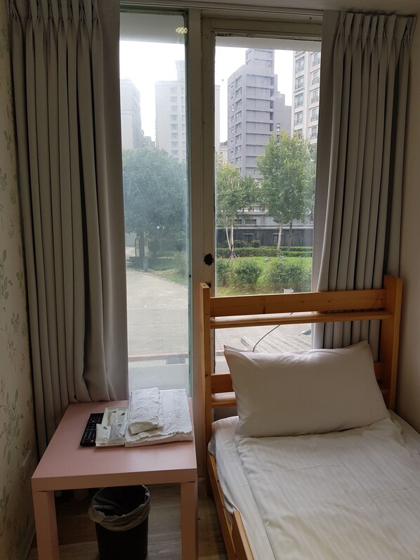 Un dormitorio con cama de madera, un escritorio pequeño con teclado y una ventana con cortinas.
