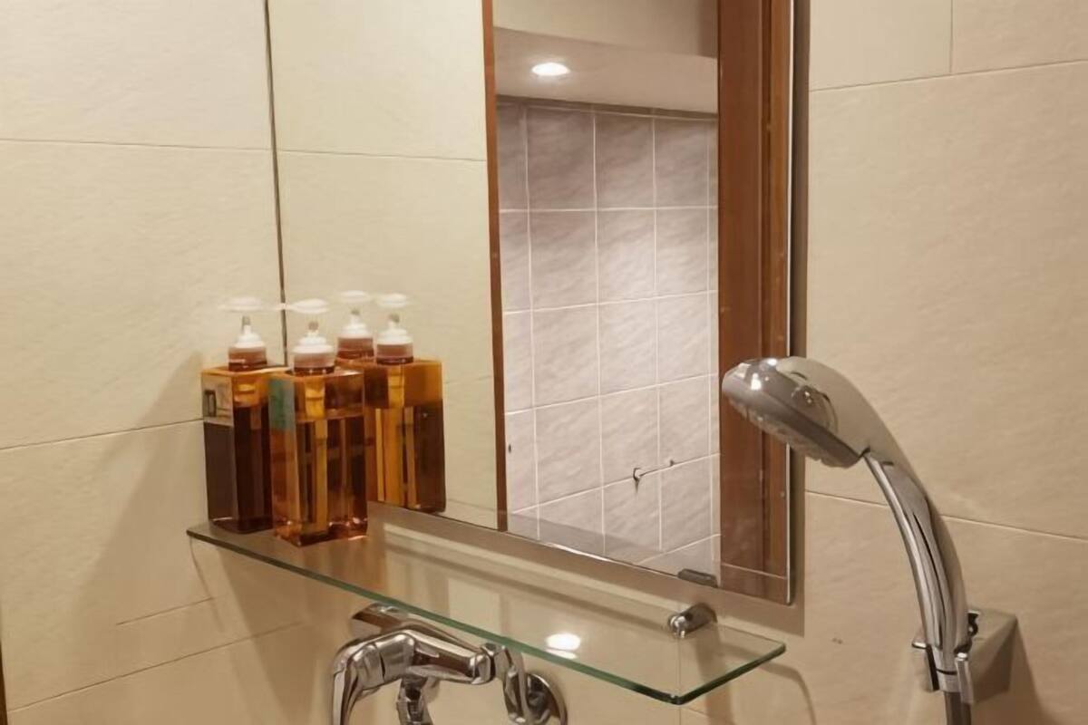 A bathroom with a glass shelf holding toiletries, a glass-enclosed sink, and a shower with a handheld showerhead.