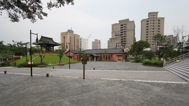 A paved plaza with a traditional pavilion, a small building, and modern high-rise buildings in the background. - Cheers Loft - Hostel (Taipei)