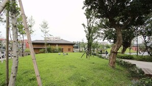 A grassy area with a traditional building, trees, and a paved path. - Cheers Loft - Hostel (Taipei)