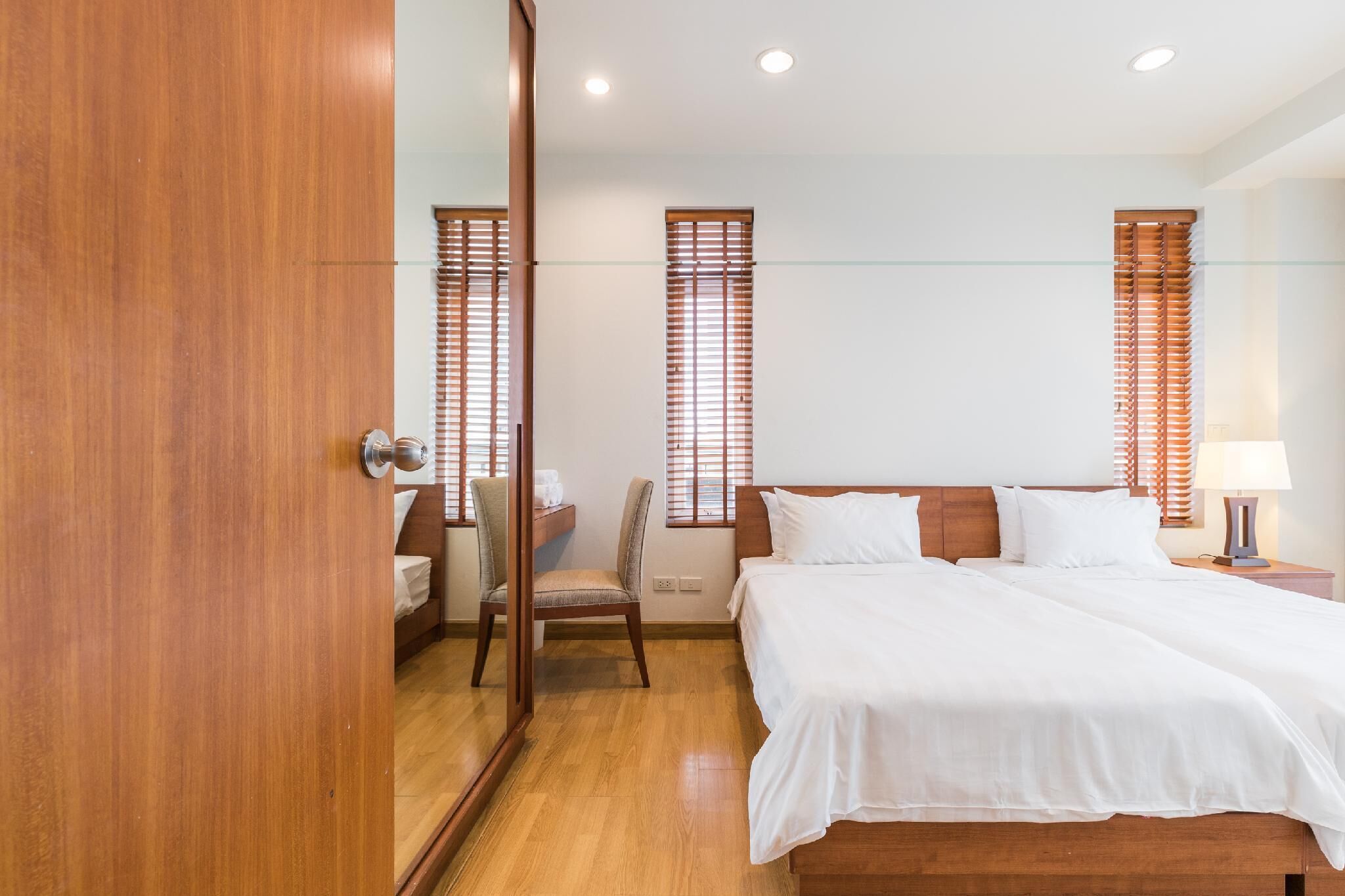 Una habitación de hotel con una cama de madera, una silla, un escritorio y dos ventanas con persianas.