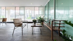 Een ruim balkon met houten banken en een tafel, grote ramen met uitzicht op gebouwen en groen.