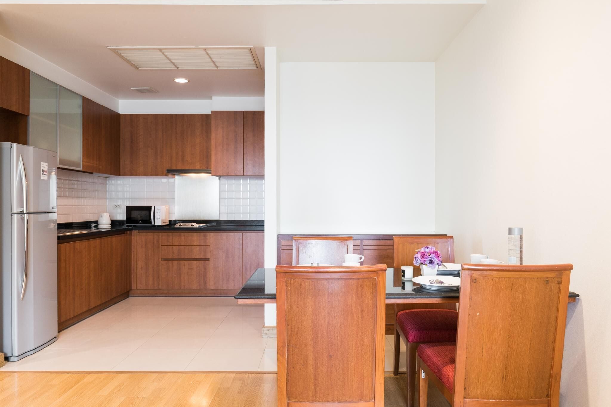 A compact kitchen with wooden cabinets, a refrigerator, a microwave, and a dining area with a table and chairs.