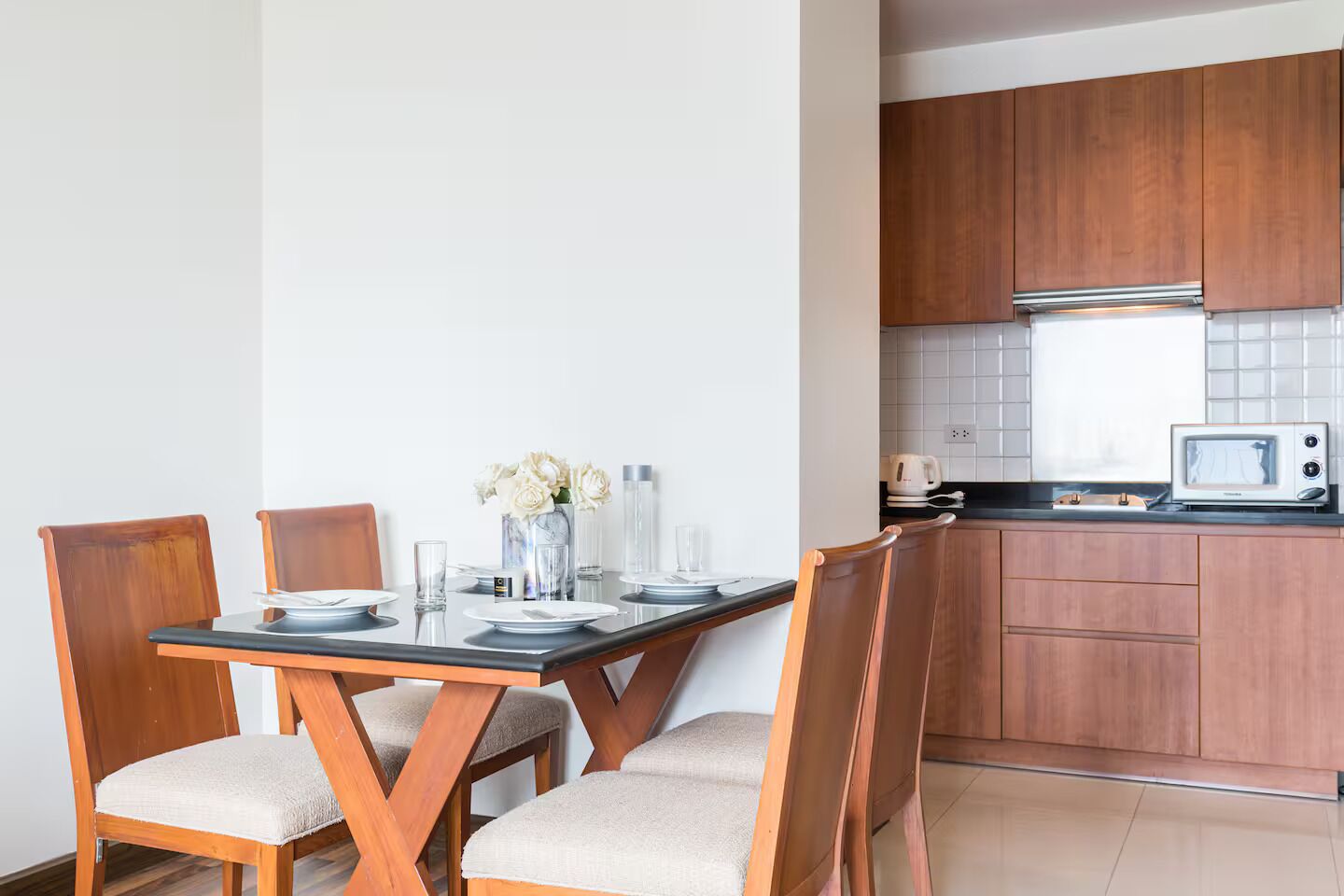 A dining area with a table set for four, wooden chairs, and a vase with flowers.