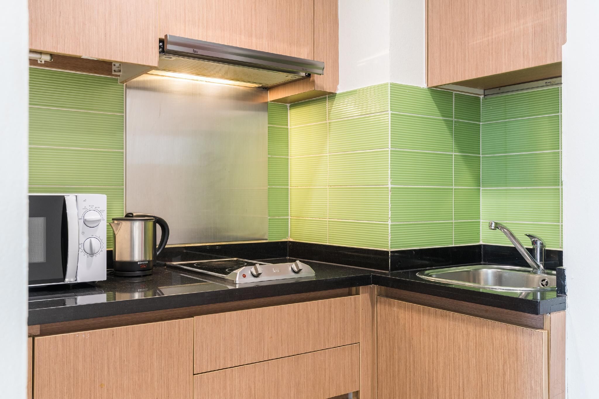 Una cocina equipada con microondas, hervidor, estufa y lavamanos.