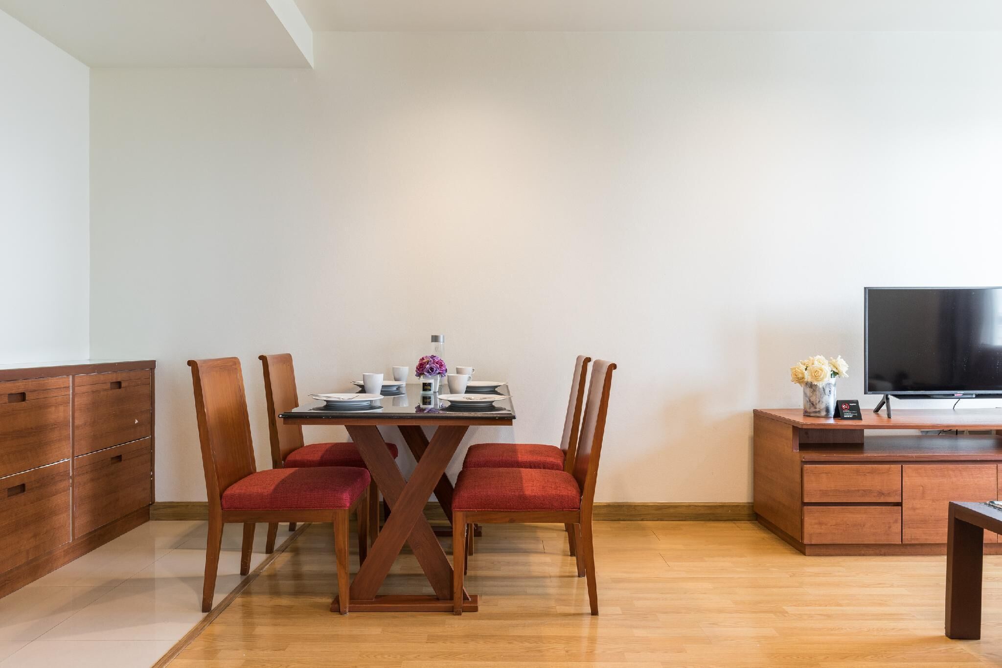 A dining area with a wooden table and chairs, a TV on a wooden stand, and a cabinet with drawers.