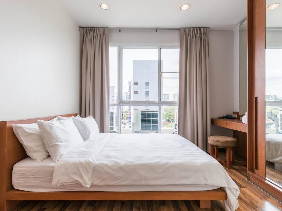 A modern hotel room with a wooden bed, a small desk, and a large window offering a city view.