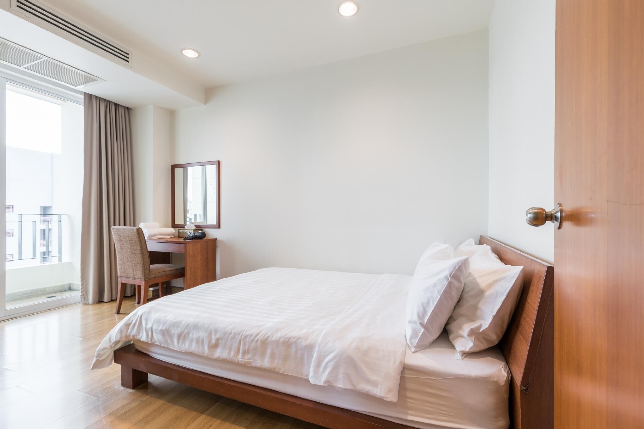 A hotel room with a bed, a desk, a chair, a large window, and a door.