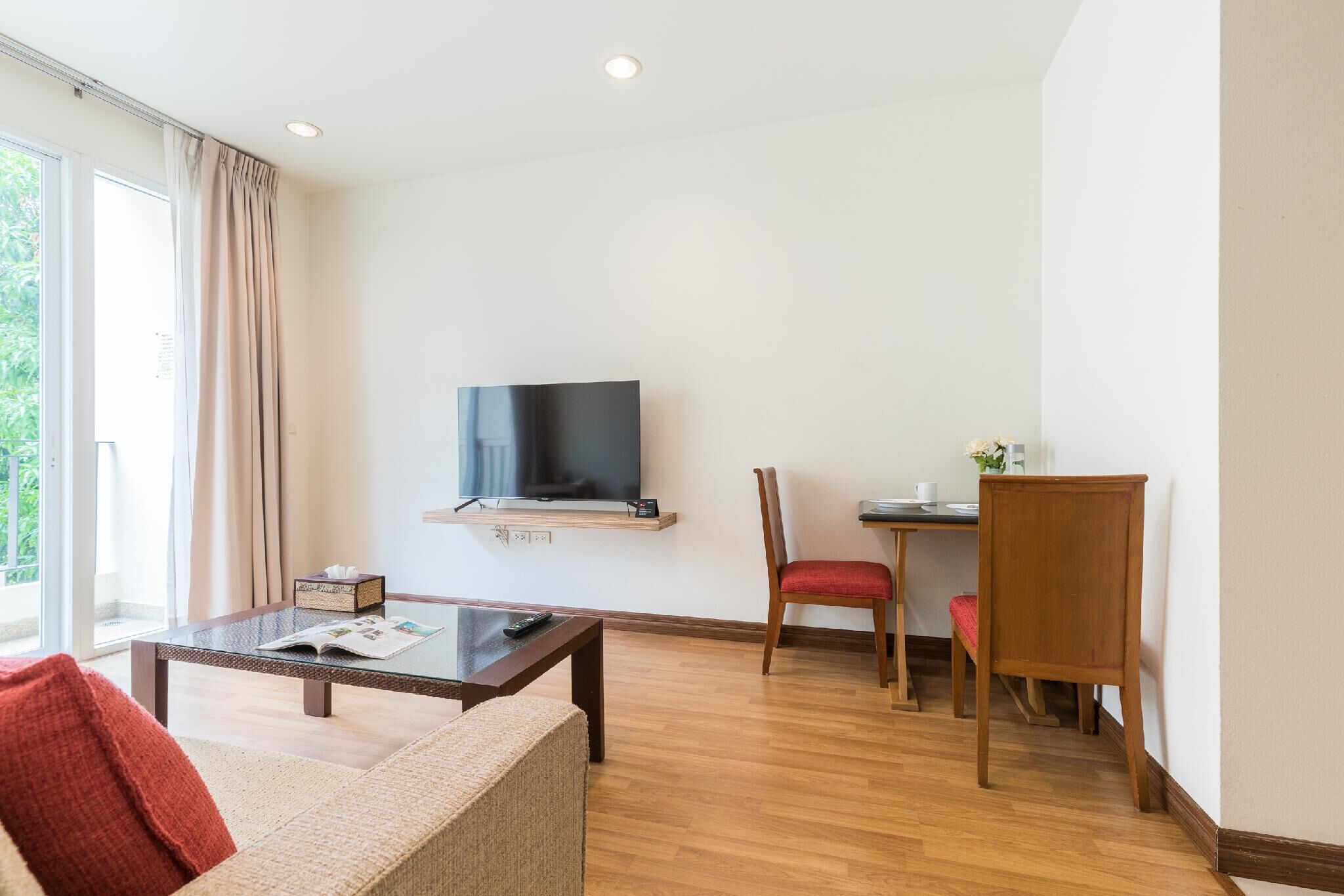 Uma sala de estar moderna com uma televisão de tela plana na parede, uma mesa de centro de madeira, uma poltrona vermelha e um sofá com uma almofada vermelha.