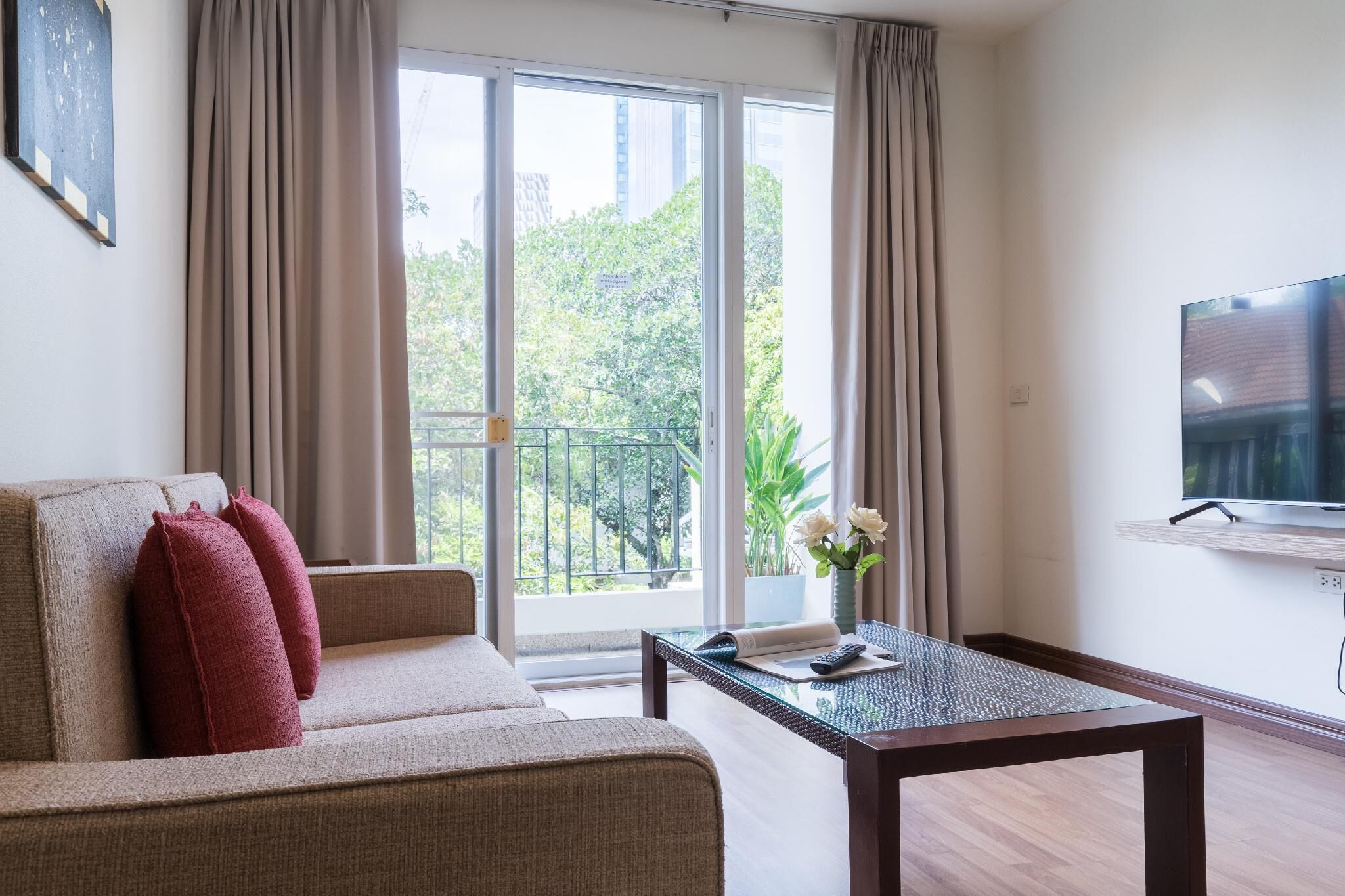 Una sala de estar moderna con sofá, mesa de centro, televisor y balcón con vistas a la vegetación.