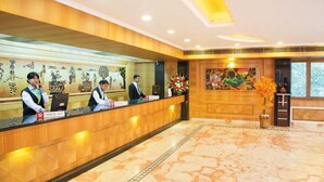 Zona de recepción de un hotel con un mostrador de madera, una mesa de salida y un mural grande en la pared.