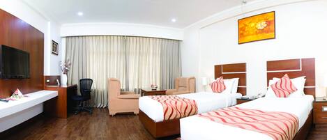 A hotel room with a desk, two beds, a TV, a chair, and a curtain.