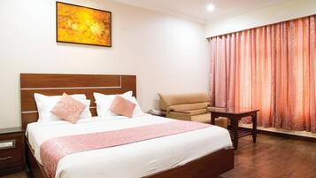 Una habitación de hotel con una cama grande, una silla, una mesita y un cuadro en la pared.