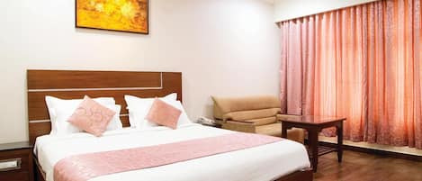 Una habitación de hotel con una cama grande, una silla, una mesita y un cuadro en la pared.
