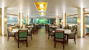 Un comedor amplio con varias mesas y sillas, ventanas grandes con vistas a la vegetación e iluminación moderna.