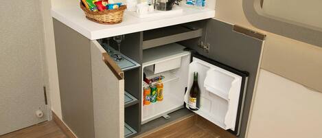 Una kitchenette compacta con refrigerador, cafetera y una pequeña encimera con botanas y bebidas.