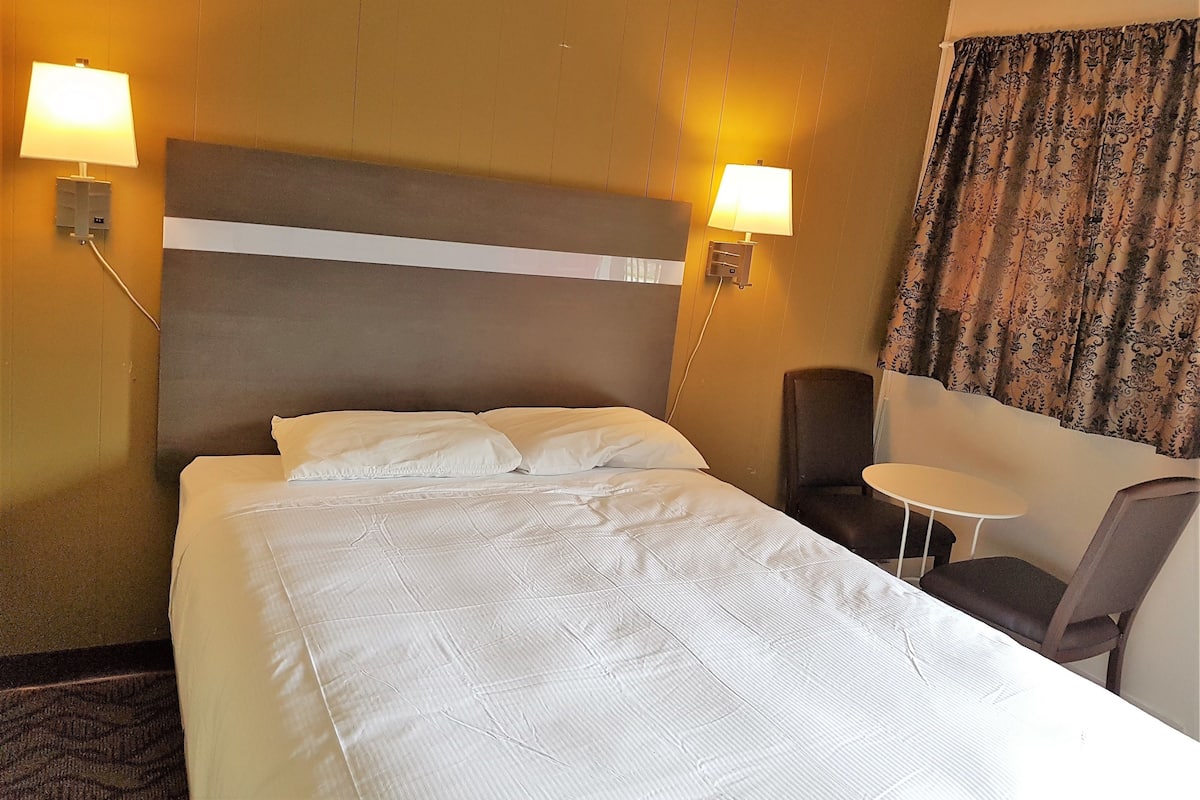 A hotel room with a large bed, two bedside lamps, a small table, and a chair.