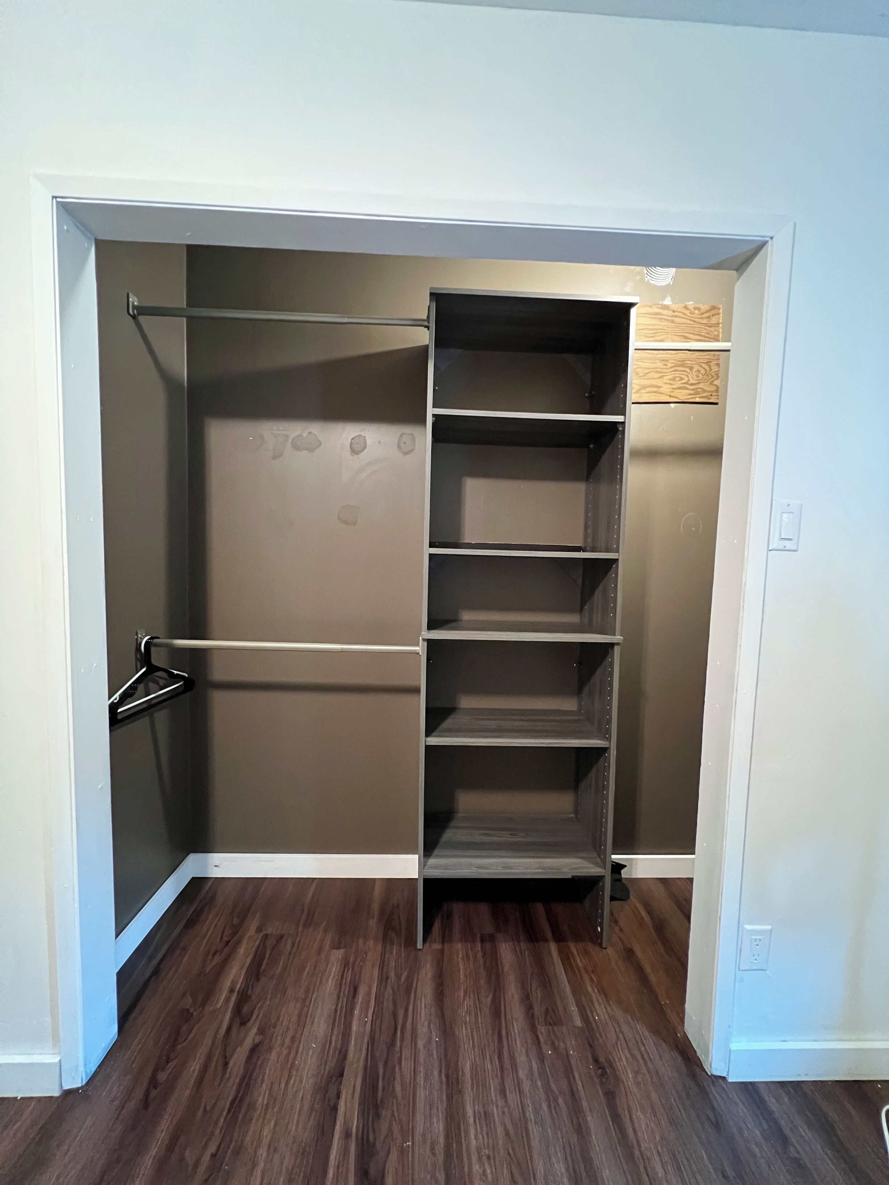 Ein begehbarer Kleiderschrank mit mehreren Regalen und einer Kleiderstange, integriert in eine Raumecke mit Holzboden.