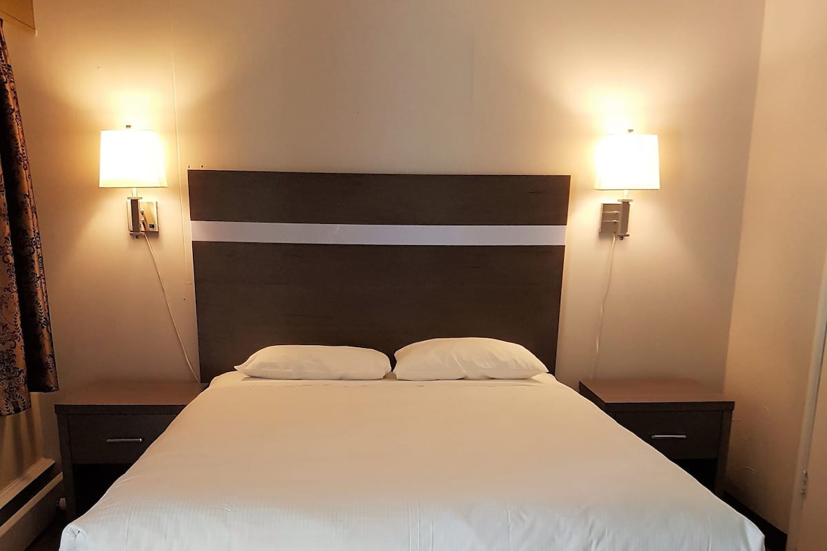 A neatly made bed with a headboard, two bedside tables, and wall-mounted lamps.