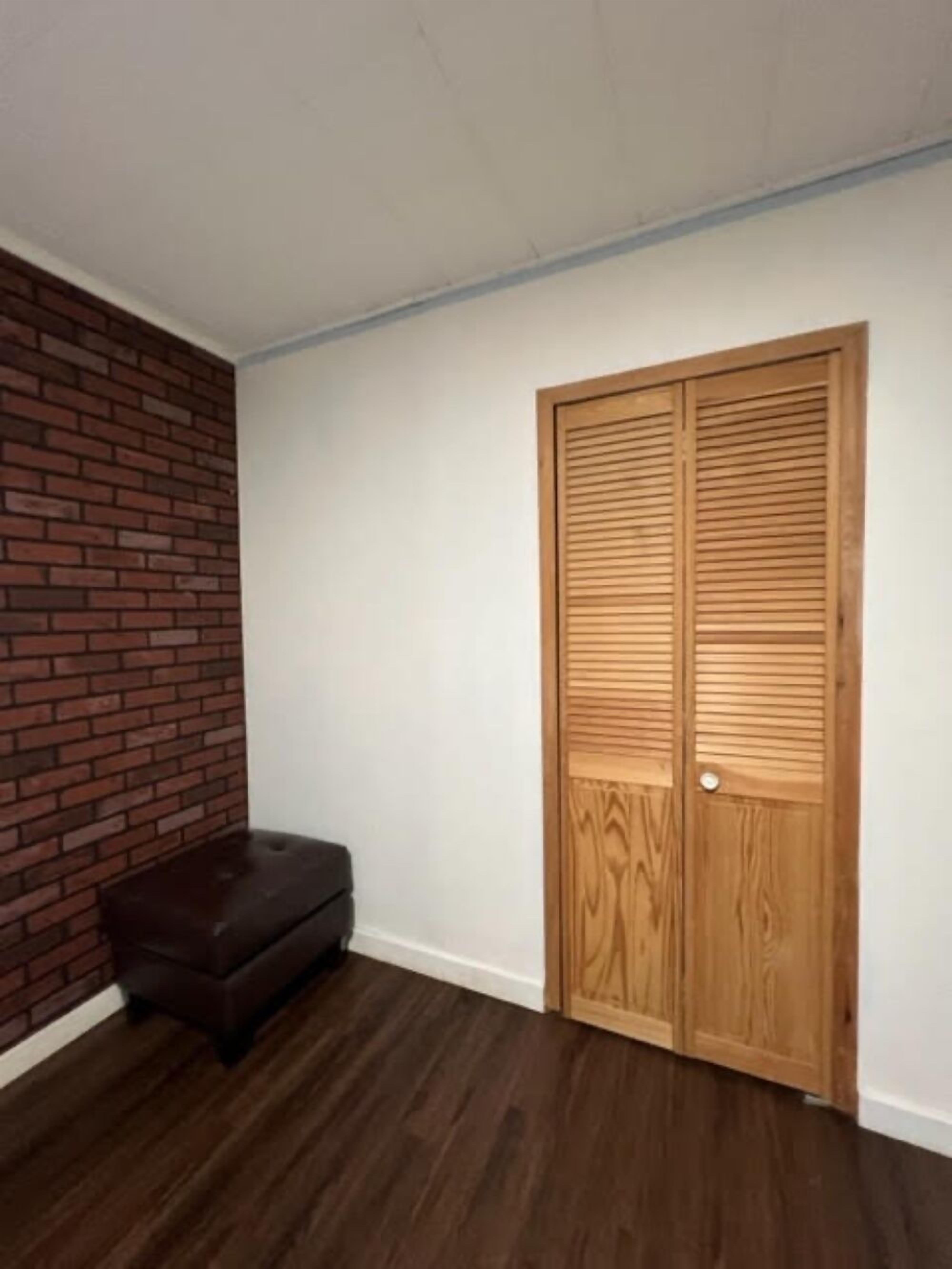 A room with a wooden floor, a brick accent wall, and a wooden double closet.
