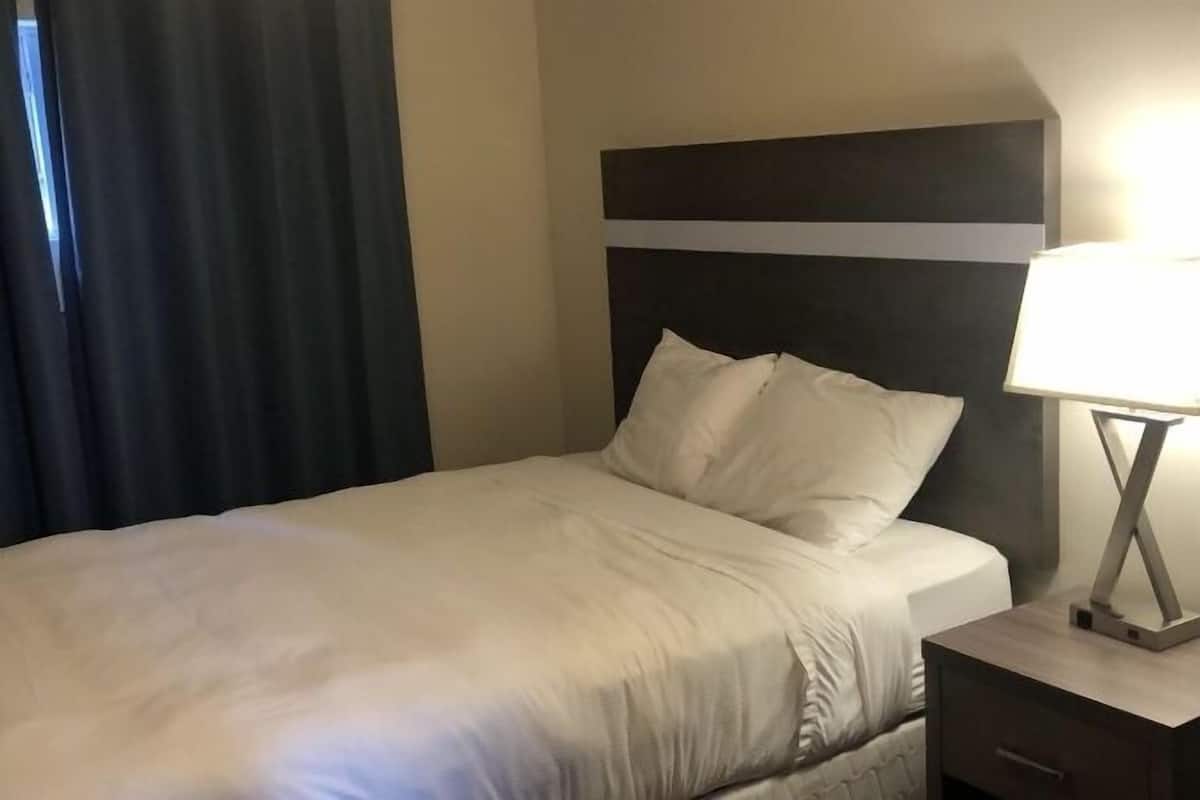 A neatly made bed with a white comforter and pillows, a bedside table with a lamp, and a dark headboard.