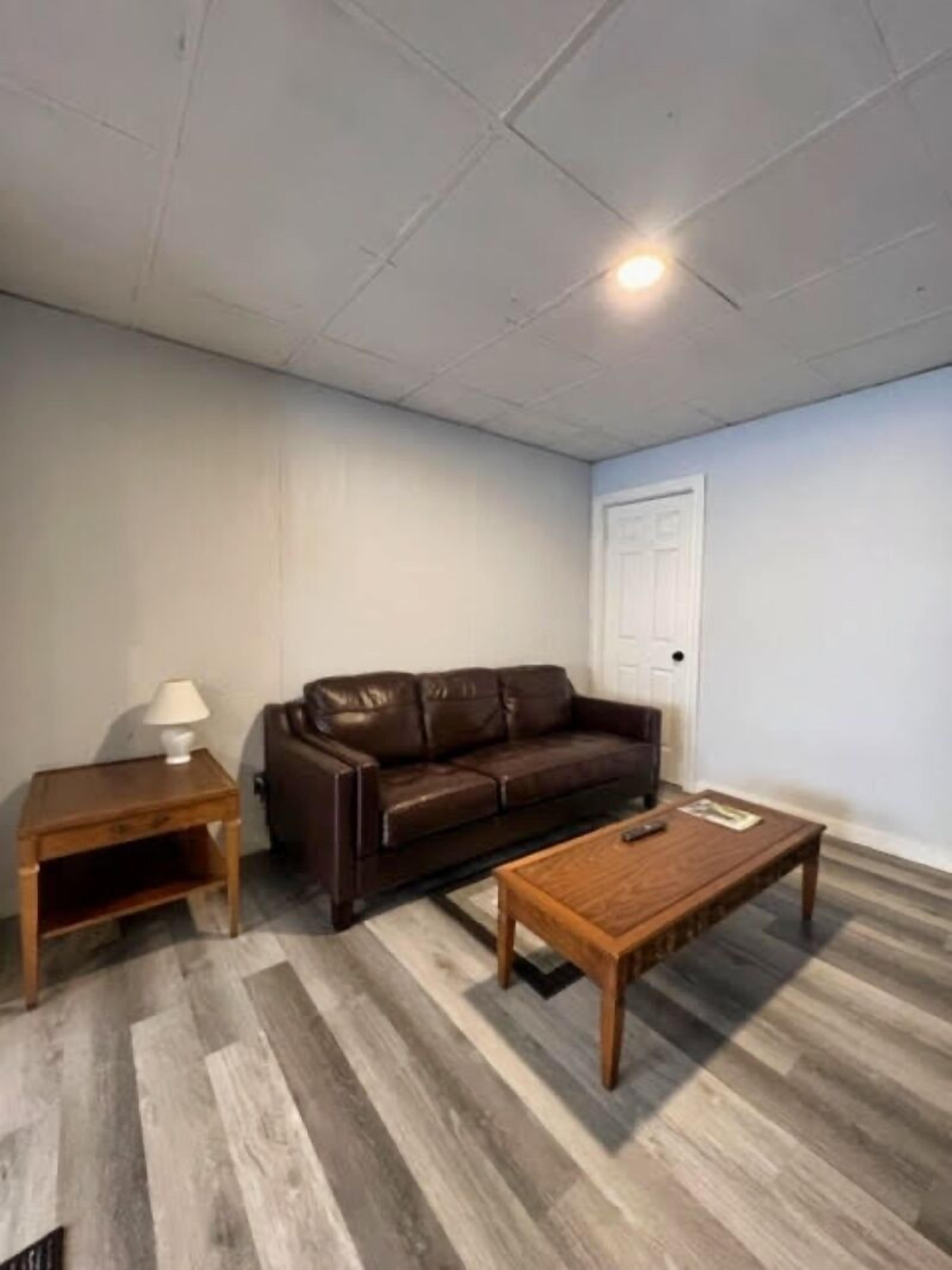 A living room with a brown leather sofa, a wooden coffee table, and a small wooden side table with a lamp.