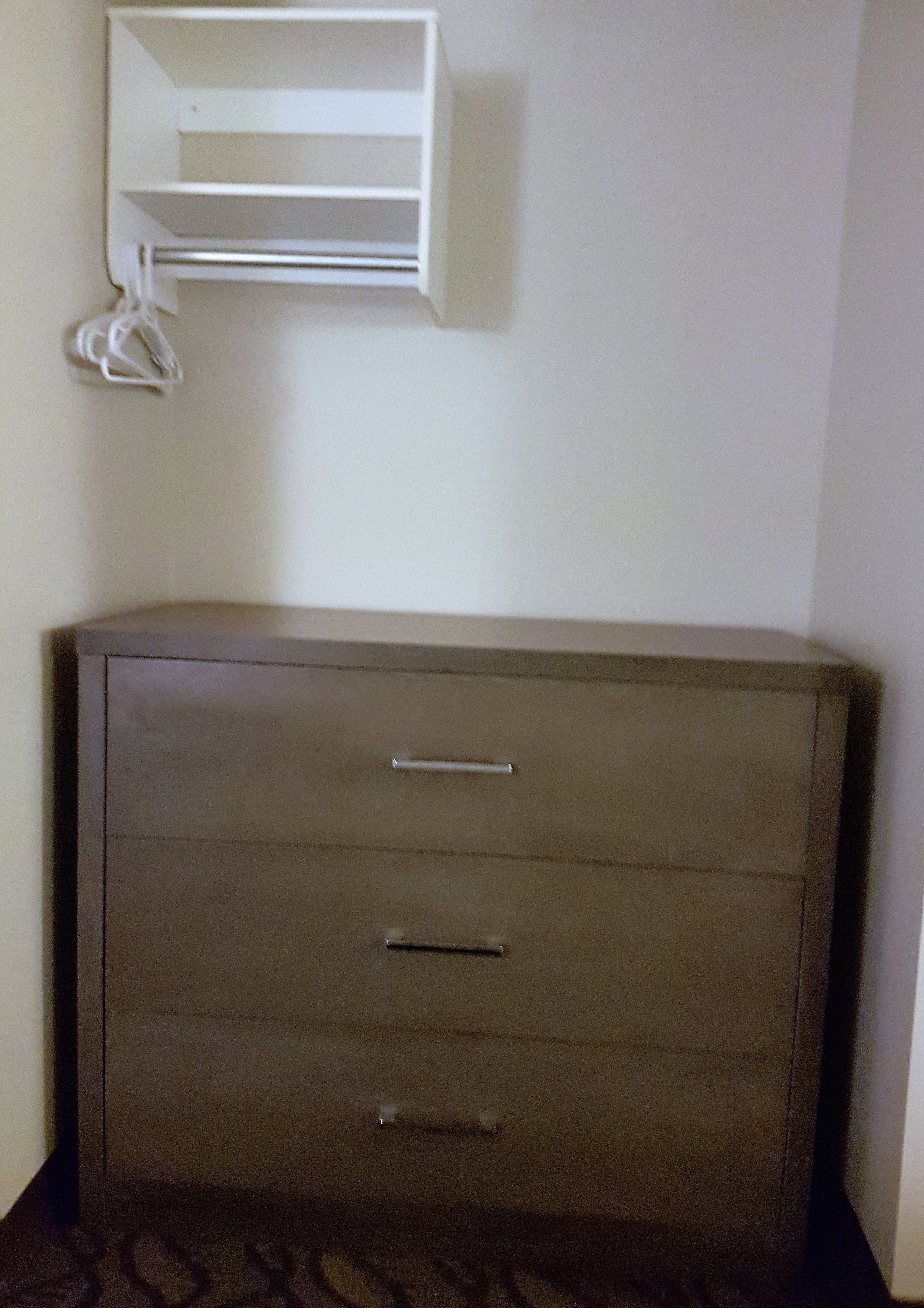 A corner room with a wardrobe, a white shelf, and a power outlet.