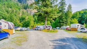 A campground with RVs and cars parked on a gravel road surrounded by trees and mountains. - Holiday Motel & RV Resort (Hope)