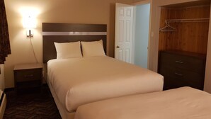 A hotel room with a large bed, a bedside table, a nightstand, a wardrobe, and a wall-mounted light. - Holiday Motel & RV Resort (Hope)
