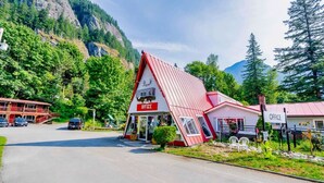A red and white office building with a sloped roof, surrounded by lush greenery and mountains in the background. - Holiday Motel & RV Resort (Hope)