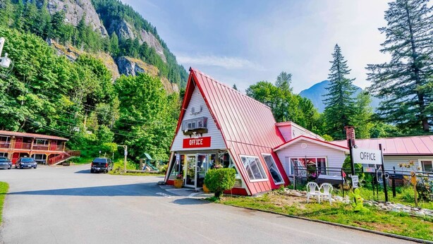 A red and white office building with a sloped roof, surrounded by lush greenery and mountains in the background. - Holiday Motel & RV Resort (Hope)
